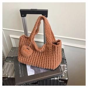 Detalle del bolso de punto color caramelo con colgante de corazón sobre maleta