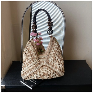 Dettaglio della borsa tote in paglia intrecciata con perle di legno e manico rotondo