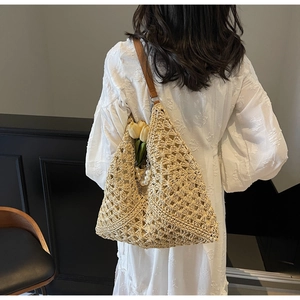 Détail d'un grand sac cabas en paille avec bandoulière en cuir brun et breloque en perles