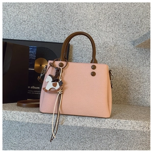 Detail of light pink tote bag with dark brown handles and wooden horse charm decoration