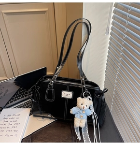 Detail of black leather tote bag with metal logo, drawstring and teddy bear charm