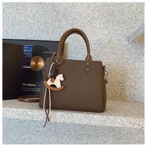 Close-up of deep brown leather tote bag with grainy texture and a rocking horse pendant