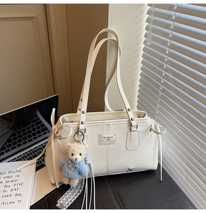 Detail of off-white faux leather tote with plush bear charm and side drawstring accents