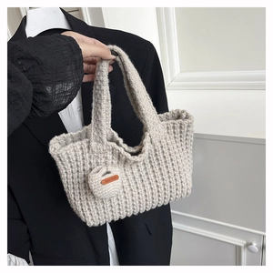 Detalle del bolso de punto beige que muestra la textura artesanal y el colgante de corazón
