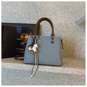 Detail of grey-blue denim texture handbag with brown leather handles and horse charm