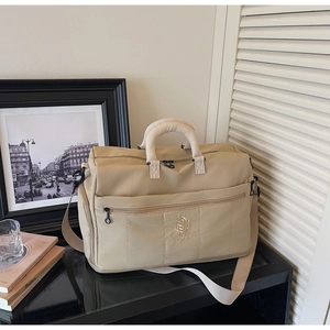 Detailed close-up of a quilted beige travel bag with handles and an adjustable shoulder strap