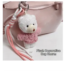 Detail eines weißen Plüschbär-Anhängers mit rosa Strickpullover an einer Tasche