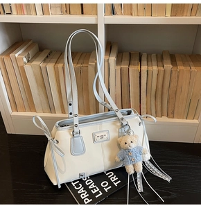 Detail of cream white faux leather shoulder bag with blue trim and cute teddy bear charm