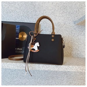 Detail of a black leather handbag with brown handles and a cute horse charm accessory