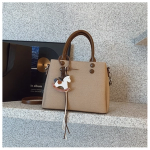 Detail of khaki tote bag with dark brown handles and cute rocking horse leather pendant