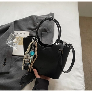 Detail of black leather bucket bag with bear pendant and stylish shoulder strap