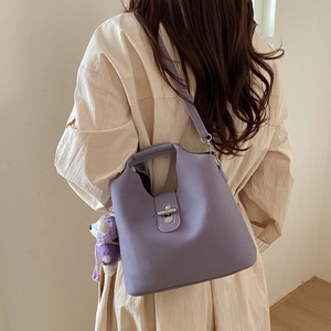 Sac seau lilas en cuir avec breloque ours tricoté porté sur une chemise beige