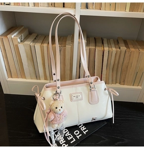 Detail of white and pink shoulder bag featuring a cute teddy bear charm and metal logo
