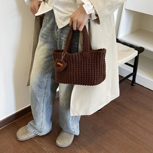 Detalle del bolso tote de punto grueso marrón oscuro con colgante de corazón y etiqueta