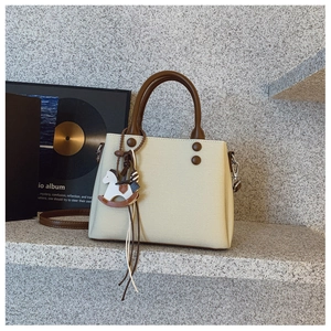 Detail of cream handbag featuring brown round handles and a wooden horse charm