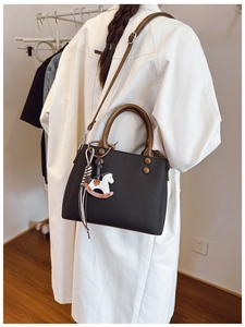Detail of black textured leather bag with brown handles and wooden horse pendant charm