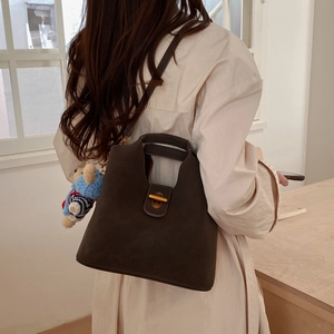 Détail du sac seau en cuir marron foncé avec fermoir doré et petit charme d'ours