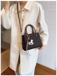 Detail of coffee brown trapezoid handbag with dual handles and white horse charm