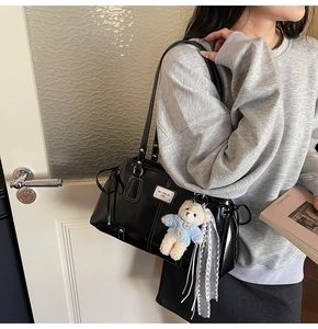 Detail of black glossy patent leather shoulder bag with plush bear charm and lace ribbon