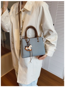 Detail of grey textured square bag with rivet accents and rocking horse charm on beige coat