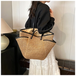 Model wearing a large straw tote bag with black leather trim and casual resort style details