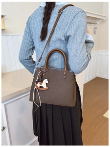 Detail of dark brown leather tote bag with decorative rivets and a rocking horse pendant