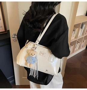 Detailed back view of a cream glossy shoulder bag with a cute plush bear charm on a model