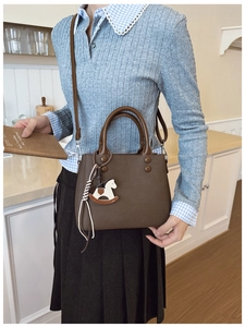 Close-up of dark brown litchi pattern handbag with a stylish wooden horse charm accessory
