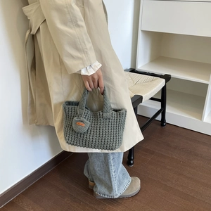 Detalle de bolso de punto gris oscuro con colgante de corazón y etiqueta de cuero