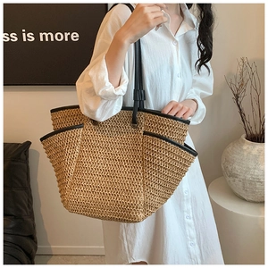 Model wearing a large straw tote bag with black leather straps and trim in a sunny room