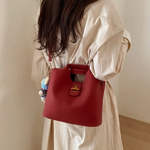 Sac seau en cuir rouge avec fermoir doré et breloque ours porté par un mannequin