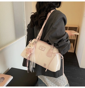 Detail of a creamy leather shoulder bag with pink trim, bow accent and teddy bear charm