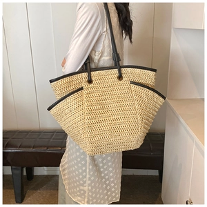 Large straw tote bag with black leather handles and woven texture worn by a model