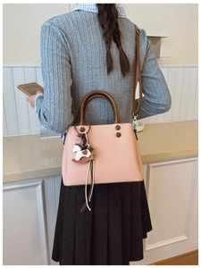 Close-up of pink crossbody bag with brown leather handles and wooden horse charm