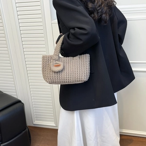 Detalle de bolso saco de punto hecho a mano con etiqueta de cuero y accesorio de mini dije