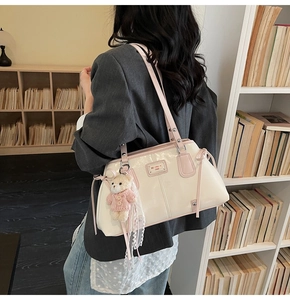 Detail of cream glossy leather tote bag with pink bow accents and cute bear charm