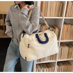 Detail view of large beige canvas travel bag with blue handles and side zipper pocket