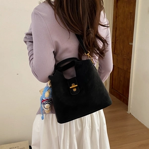 Gros plan d'un sac seau noir mat avec un fermoir doré et un pendentif ours en peluche