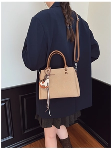 Khaki fabric handbag with brown leather straps and a wooden horse charm on a model
