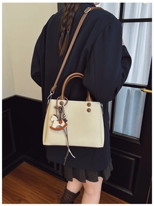 Detail of beige canvas tote bag with brown leather straps and wooden rocking horse charm