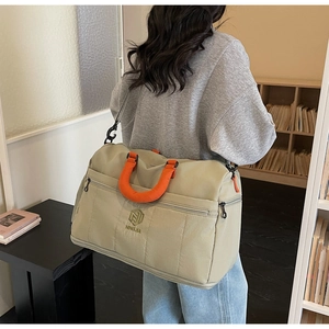 Detail of khaki travel duffel bag with orange handles worn by a person in a cozy room
