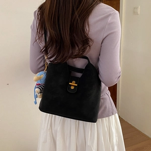 Détail du sac à main en daim noir avec fermoir doré et charme d'ours sur mannequin