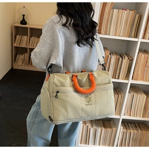 Quilted khaki travel bag with orange handles shown in a casual lifestyle setting