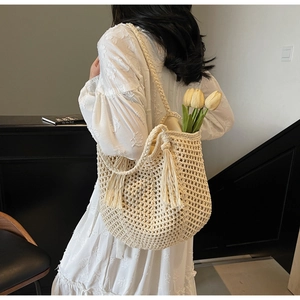 Detail of hollow mesh woven shoulder bag in beige with decorative tassel accents