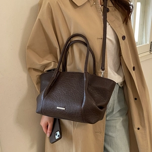 Detalle de bolso tote de cuero marrón oscuro con textura vintage llevado con una gabardina