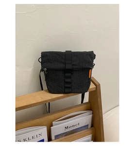 Détail du sac bandoulière en nylon ripstop noir avec motif quadrillé et étiquette orange