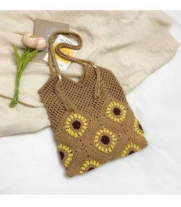 Detailed close-up of handmade sunflower knit tote bag with tassel accents on woven straps