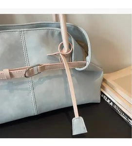 Détail du sac cabas bleu pastel montrant les anses roses et l'anneau en D métallique