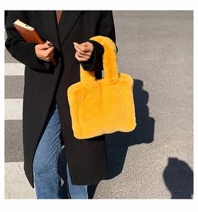 Close-up of fluffy yellow faux fur tote bag held against a stylish black coat