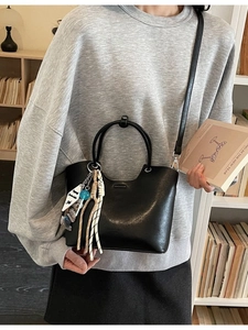 Minimalist black bucket bag with bead charms shown in an indoor library setting